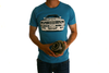 Front view of model wearing "Maxine E30" shirt in aqua blue. The front of the shirt design features the front view of a white BMW E30. The model is holding a wheel bearing.