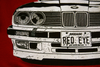Closeup of the shirt design. The front of the E30 shows rock chips and scratches, showing that the car is driven. The license plate reads "RED EYE".